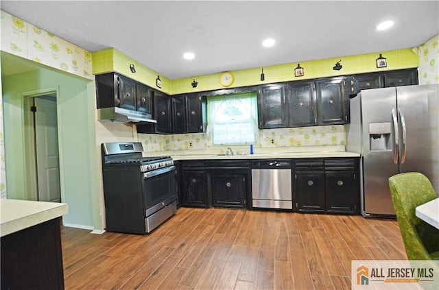 20 Rath Ln, East Brunswick, NJ 08816 - kitchen featuring appliances with stainless steel finishes, dark cabinetry, wood finished floors, under cabinet range hood, and light countertops