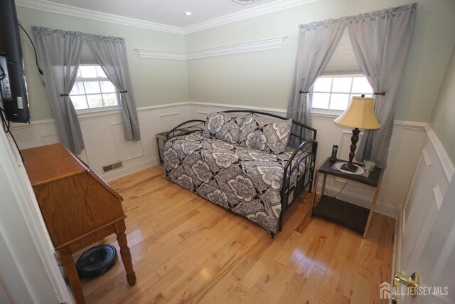 bedroom with a wainscoted wall, crown molding, wood finished floors, and visible vents