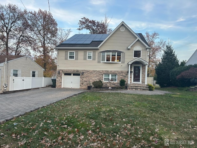 view of front of house with fence, an attached garage, stone siding, decorative driveway, and roof mounted solar panels