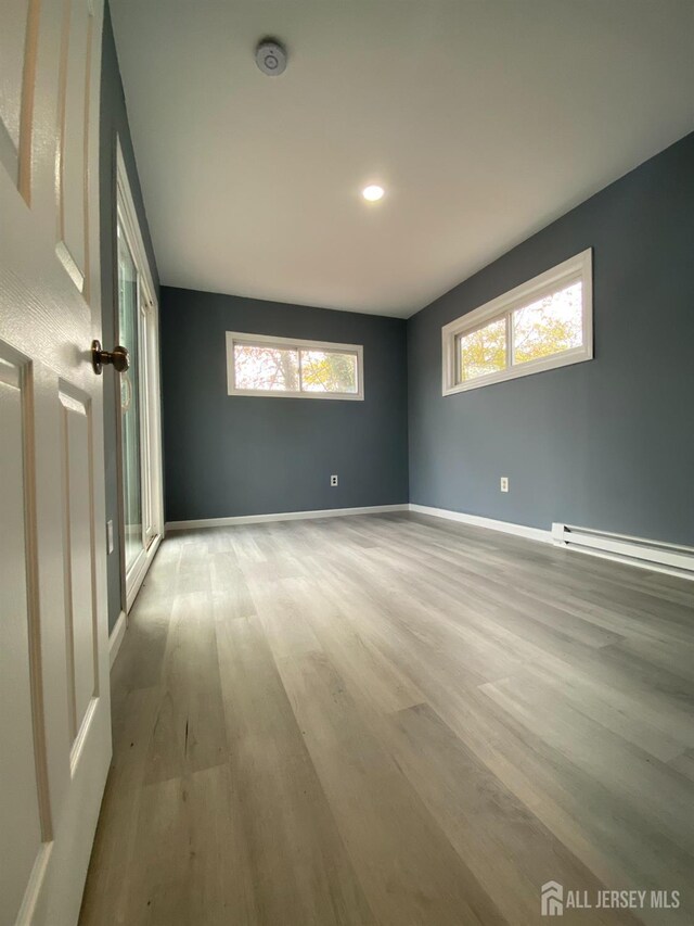 empty room with baseboard heating, a healthy amount of sunlight, and light wood-type flooring