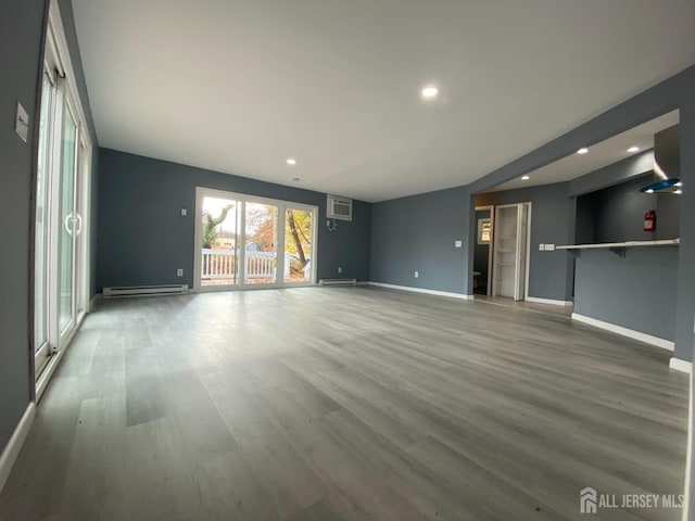 unfurnished living room featuring hardwood / wood-style flooring, a wall unit AC, and baseboard heating