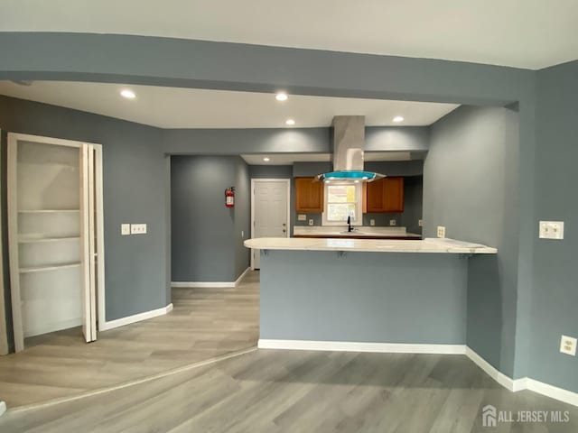 kitchen with sink, a breakfast bar, light hardwood / wood-style floors, island exhaust hood, and kitchen peninsula