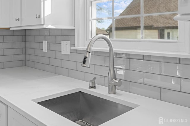 interior details with decorative backsplash, white cabinetry, sink, and light stone countertops