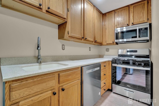 kitchen featuring light tile patterned flooring, light stone countertops, a sink, and appliances with stainless steel finishes