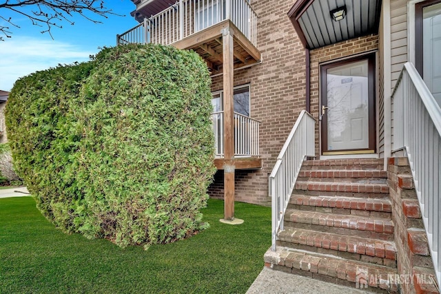 view of exterior entry featuring brick siding, a balcony, and a lawn