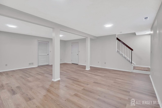 finished basement featuring stairway, visible vents, light wood-style flooring, and baseboards