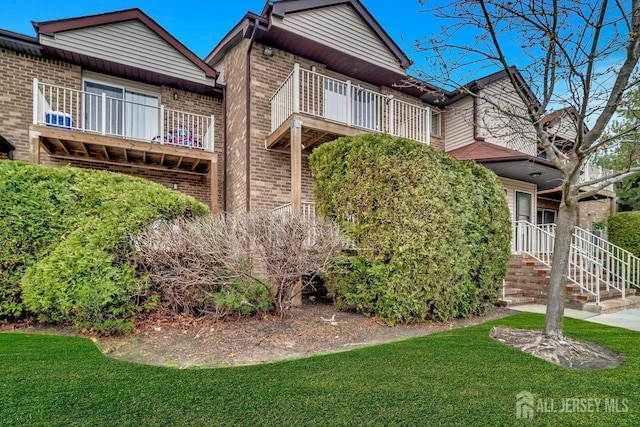 view of front of home with a front yard, a balcony, and brick siding