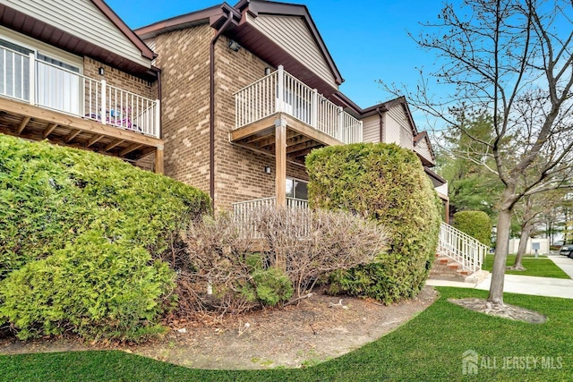 view of property exterior with a yard, a balcony, and brick siding