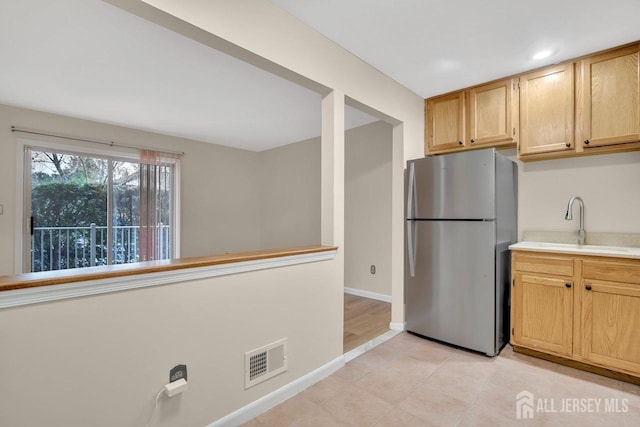 kitchen featuring a sink, light countertops, visible vents, baseboards, and freestanding refrigerator