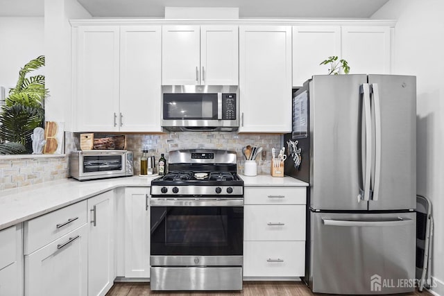 kitchen with light stone counters, appliances with stainless steel finishes, backsplash, white cabinetry, and a toaster