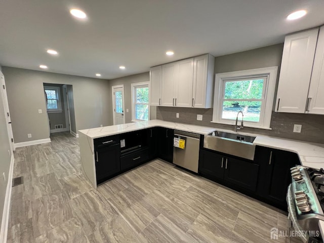 kitchen with a peninsula, a sink, appliances with stainless steel finishes, dark cabinetry, and light stone countertops