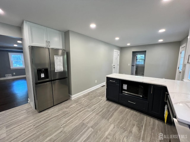 kitchen featuring dark cabinets, white cabinetry, baseboards, stainless steel refrigerator with ice dispenser, and light stone countertops