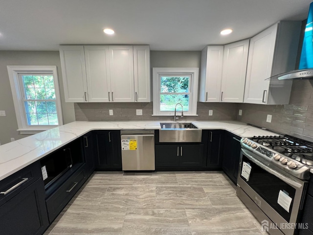 kitchen with wall chimney exhaust hood, appliances with stainless steel finishes, a sink, and dark cabinets