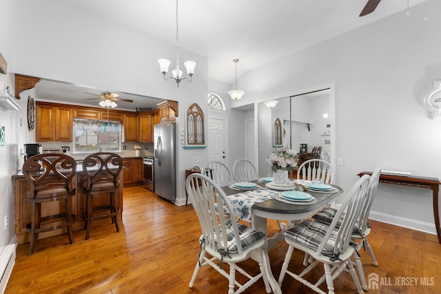 dining room with high vaulted ceiling, light wood-style flooring, and ceiling fan with notable chandelier