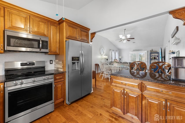 kitchen with vaulted ceiling, appliances with stainless steel finishes, light wood-type flooring, brown cabinets, and tasteful backsplash