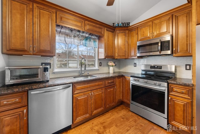 kitchen featuring a toaster, light wood-style flooring, appliances with stainless steel finishes, brown cabinetry, and a sink