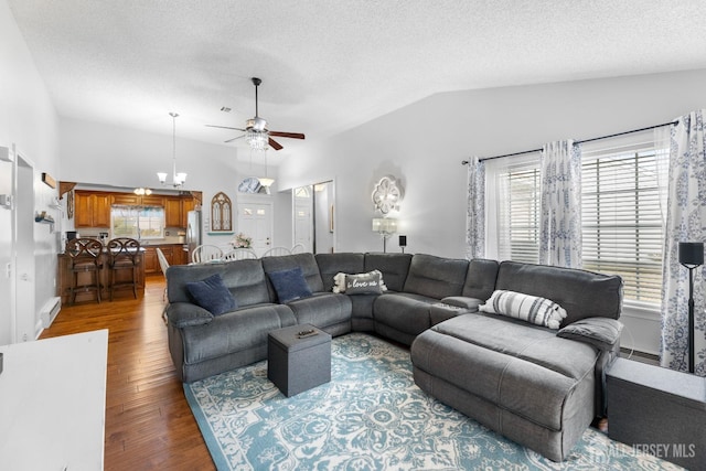 living area with a baseboard radiator, wood finished floors, vaulted ceiling, a textured ceiling, and ceiling fan with notable chandelier