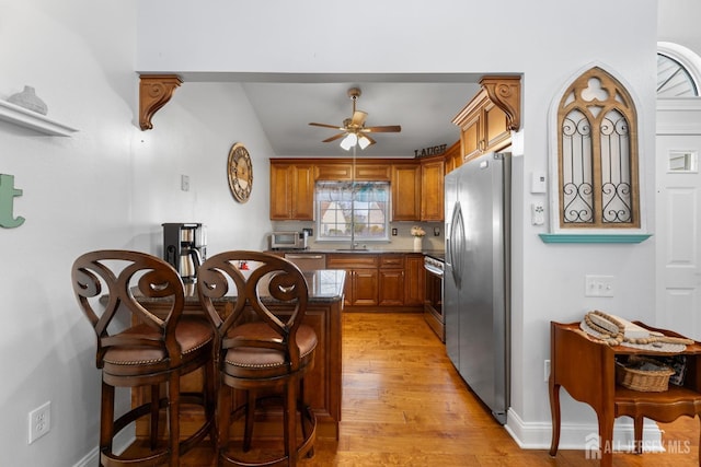 kitchen featuring appliances with stainless steel finishes, brown cabinets, a breakfast bar, light wood-style floors, and a sink