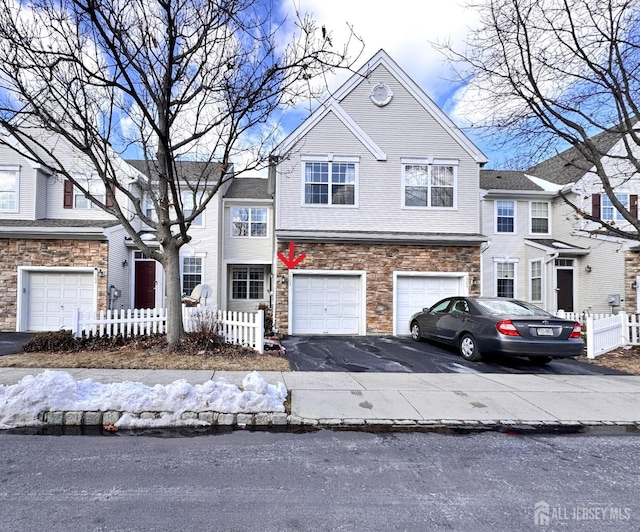 view of front of house featuring driveway, stone siding, a garage, and fence