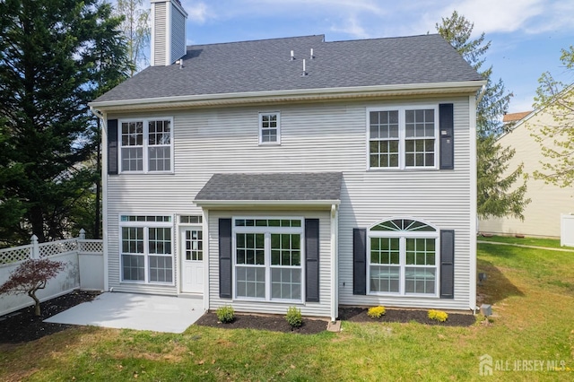 rear view of house featuring a chimney, fence, a lawn, a shingled roof, and a patio area