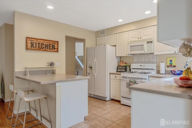 441 Sayre Dr, Plainsboro, NJ 08540 - kitchen with white appliances, a peninsula, a sink, a breakfast bar area, and light countertops