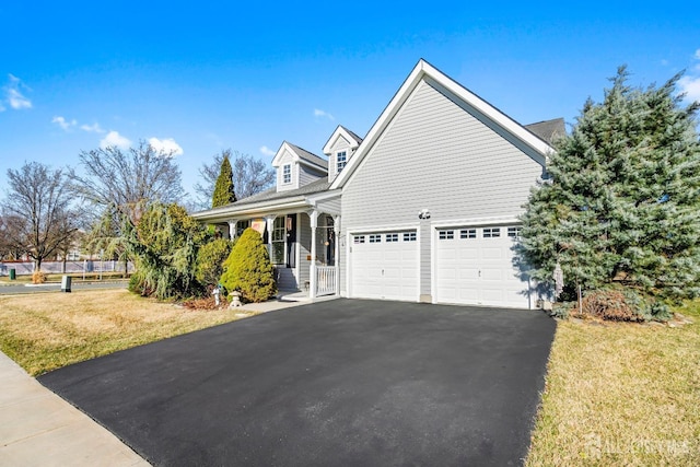 view of side of property featuring a garage, a lawn, covered porch, and driveway