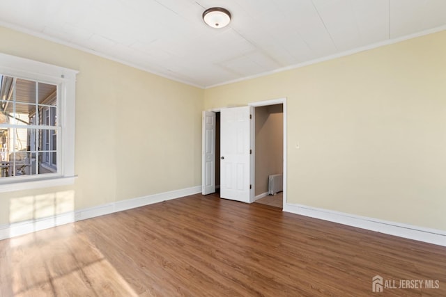 spare room featuring radiator, crown molding, baseboards, and wood finished floors