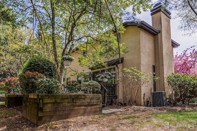 view of property exterior with central AC unit, stucco siding, and a chimney