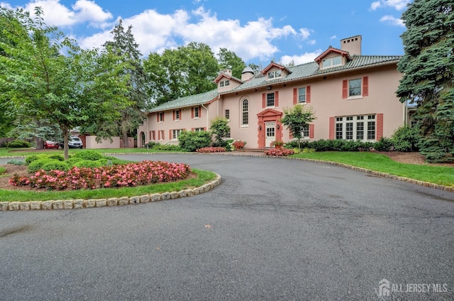 view of front of home with curved driveway, stucco siding, and a chimney