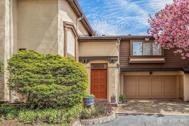 entrance to property featuring a garage, aphalt driveway, and stucco siding