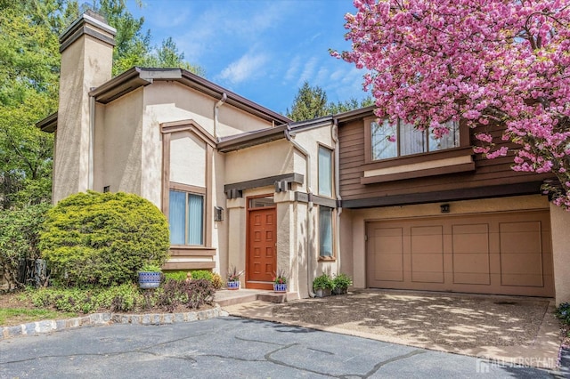view of front of house with a chimney, an attached garage, stucco siding, and aphalt driveway