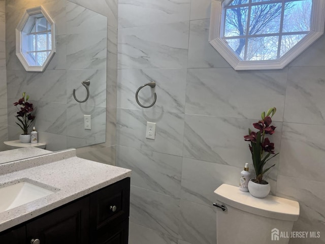 bathroom featuring toilet, vanity, and tile walls