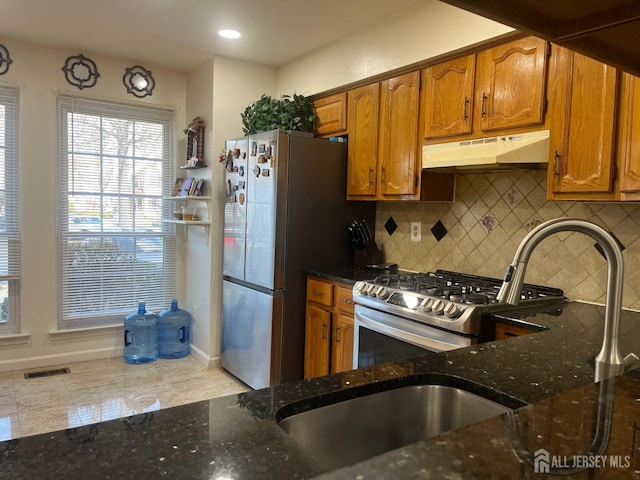 kitchen with under cabinet range hood, stainless steel appliances, visible vents, brown cabinets, and dark stone counters