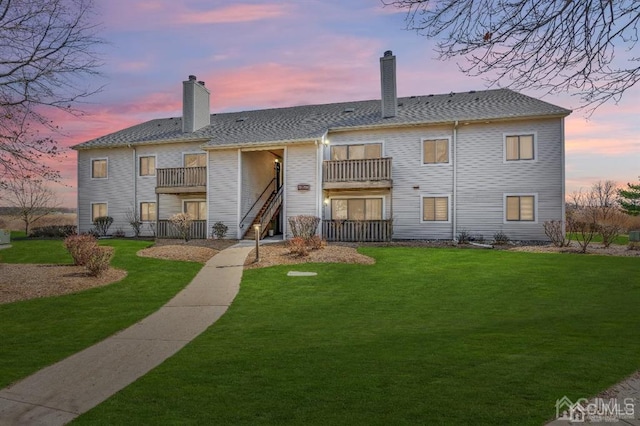 back house at dusk with a lawn and a balcony