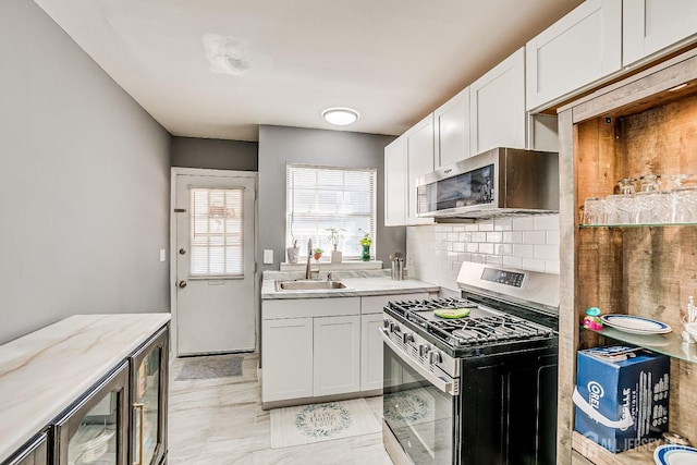 kitchen featuring stainless steel appliances, white cabinets, a sink, decorative backsplash, and beverage cooler