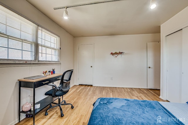 bedroom with light wood-style floors, rail lighting, baseboards, an office area, and a closet