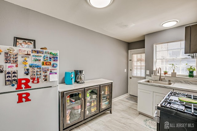 kitchen with freestanding refrigerator, a sink, gas range, and light countertops