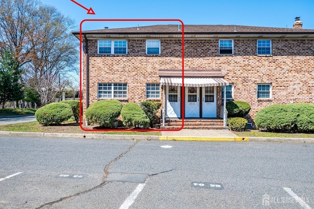 view of front of property featuring entry steps, uncovered parking, brick siding, and a chimney