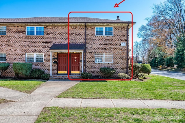 view of front of home with brick siding, a front lawn, and a chimney