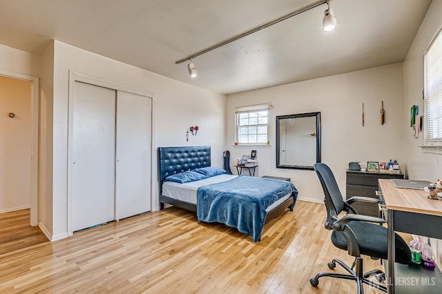 bedroom featuring rail lighting, light wood-type flooring, a desk, a closet, and baseboards