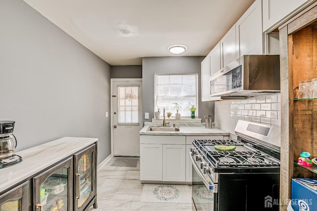 kitchen featuring stainless steel appliances, a sink, white cabinetry, backsplash, and baseboards