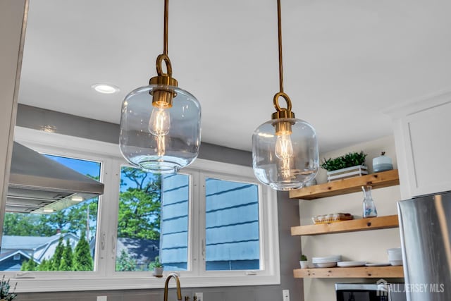 kitchen view of a chandelier, open shelves, white cabinets, stainless steel appliances, and hanging light fixtures