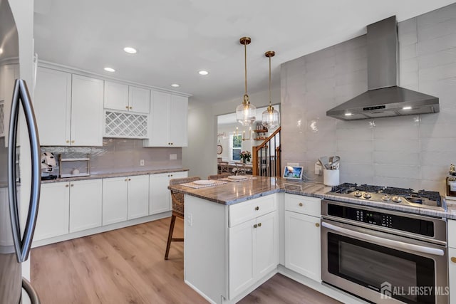 1307 Camp Ave, Ocean, NJ 07712 - kitchen featuring appliances with stainless steel finishes, wall chimney exhaust hood, a peninsula, decorative backsplash, and white cabinets