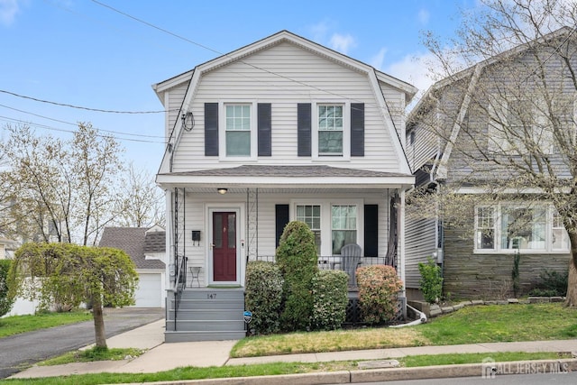 front facade featuring a garage, covered porch, and a front yard