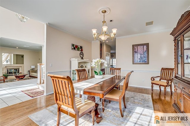 27 Revere Ct, West Windsor, NJ 08550 - dining area featuring crown molding, a chandelier, light wood-type flooring, a glass covered fireplace, and baseboards