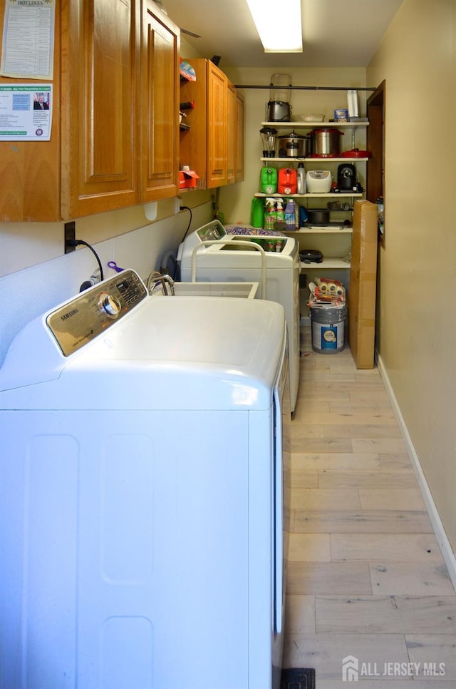 clothes washing area with light wood-style floors, cabinet space, independent washer and dryer, and baseboards