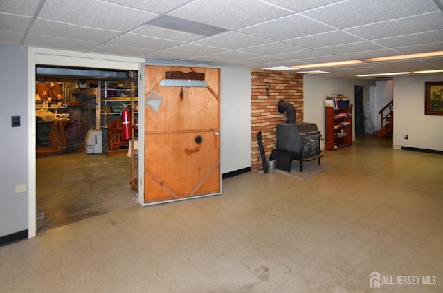 finished basement with stairway, a paneled ceiling, a wood stove, and baseboards