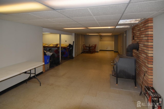 finished basement featuring tile patterned floors, a wood stove, and a drop ceiling