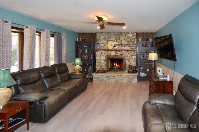 living area with wood finished floors, a ceiling fan, and a stone fireplace
