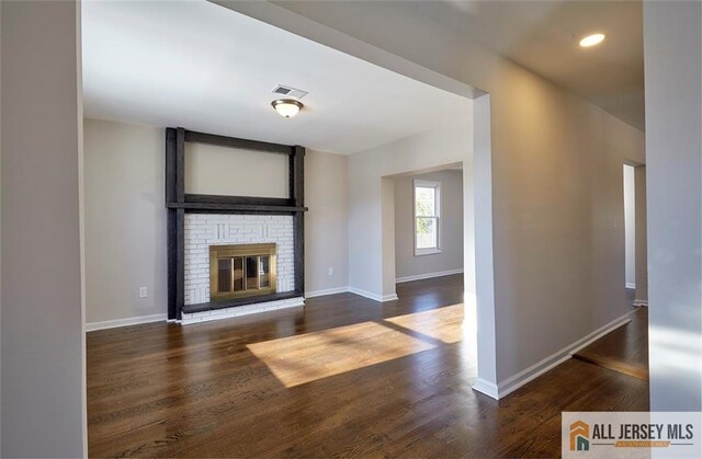 unfurnished living room featuring dark hardwood / wood-style flooring and a brick fireplace